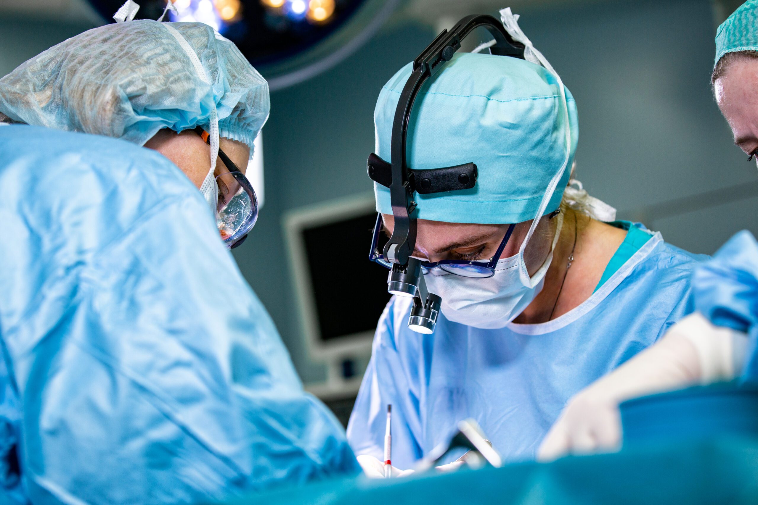 Surgeon and his assistant performing cosmetic surgery in hospital operating room. Surgeon in mask wearing loupes during medical procadure